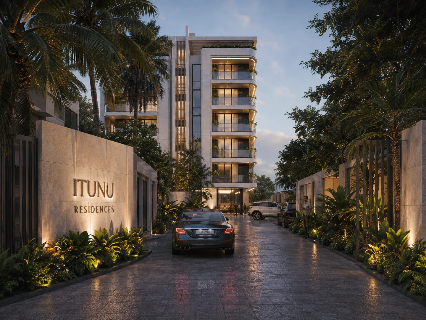 View down the entry driveway toward the building, 'ITUNU RESIDENCES' wall signage on the left, arriving car mid-driveway, lit landscaping either side.