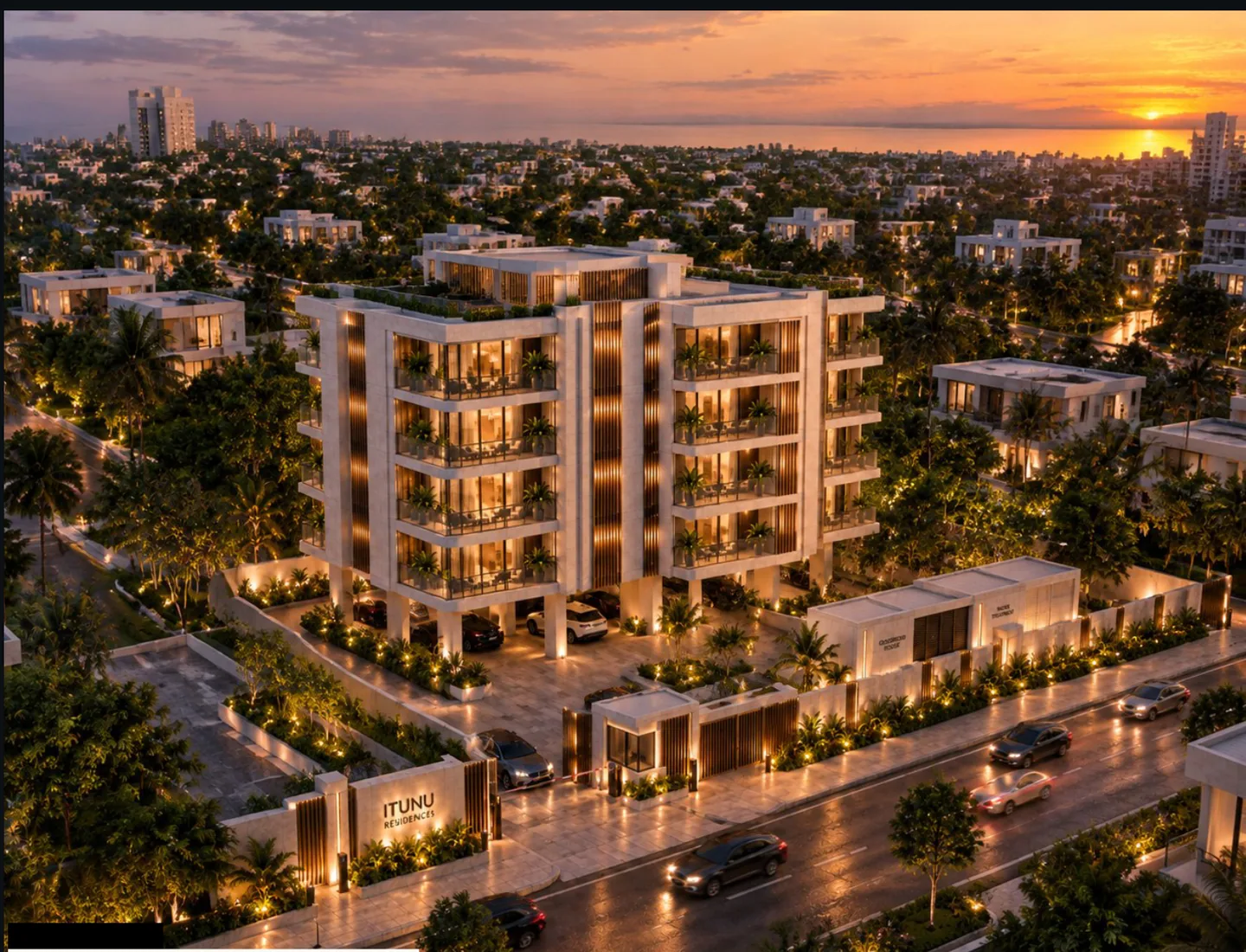 Aerial at sunset showing the building in its neighbourhood context, the sun low on the horizon, the whole ground plate open for parking beneath the residential floors, boundary landscaping and the monument signage at the street.